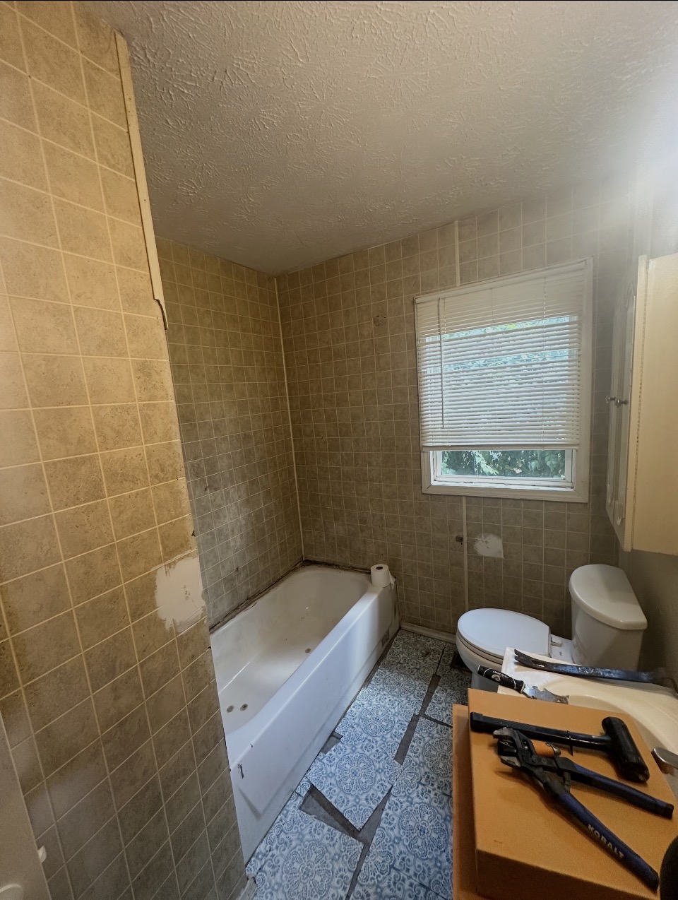 Dated Indianapolis bathroom with beige wall tile, old jetted tub, and patterned vinyl floor before remodeling