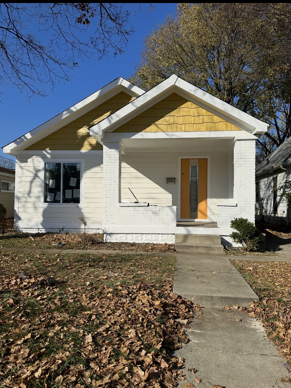 Completed Indianapolis bungalow exterior with white lap siding, yellow gable shakes, and a yellow front door