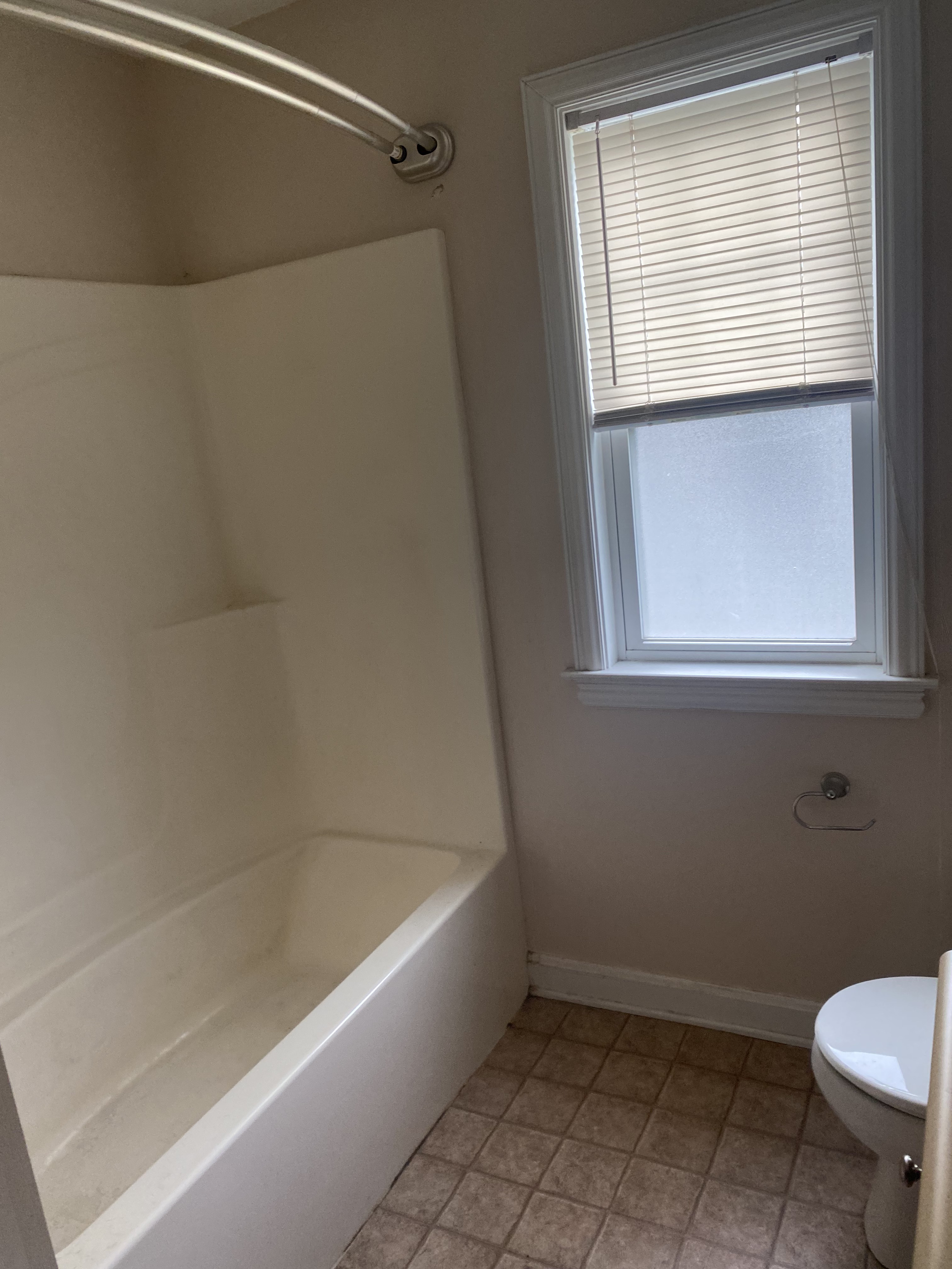 Dated Indianapolis bathroom with fiberglass tub surround, curtain rod, and worn vinyl floor tile before remodeling